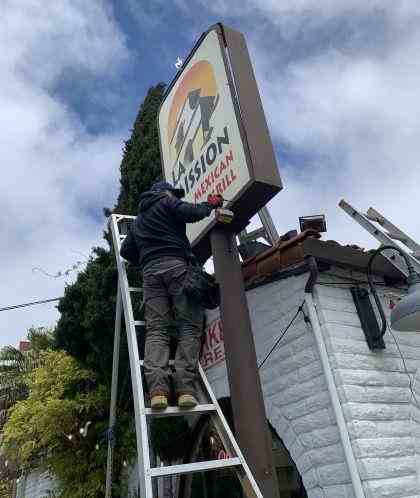 A signage installation expert is constructing backlit outdoor signage for a customer.