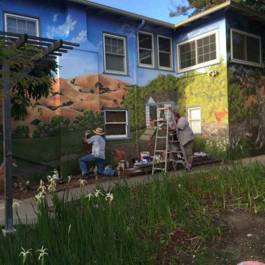 Experienced mural painters transforming an unattractive home exterior into a beautiful nature setting using durable and vibrant paint.