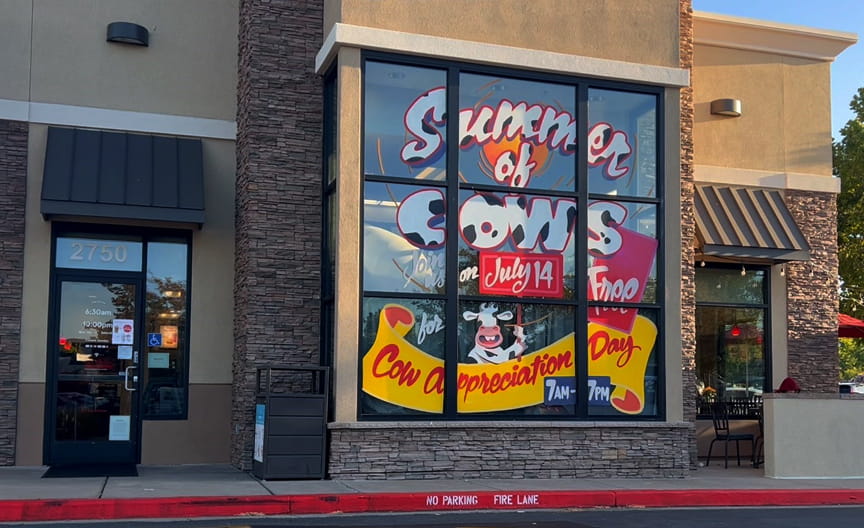 Hand-painted Summer of Cows window display on the front of the Walnut Creek Chick-fil-A, with a cow mascot and Cow Appreciation Day banner painted across the glass